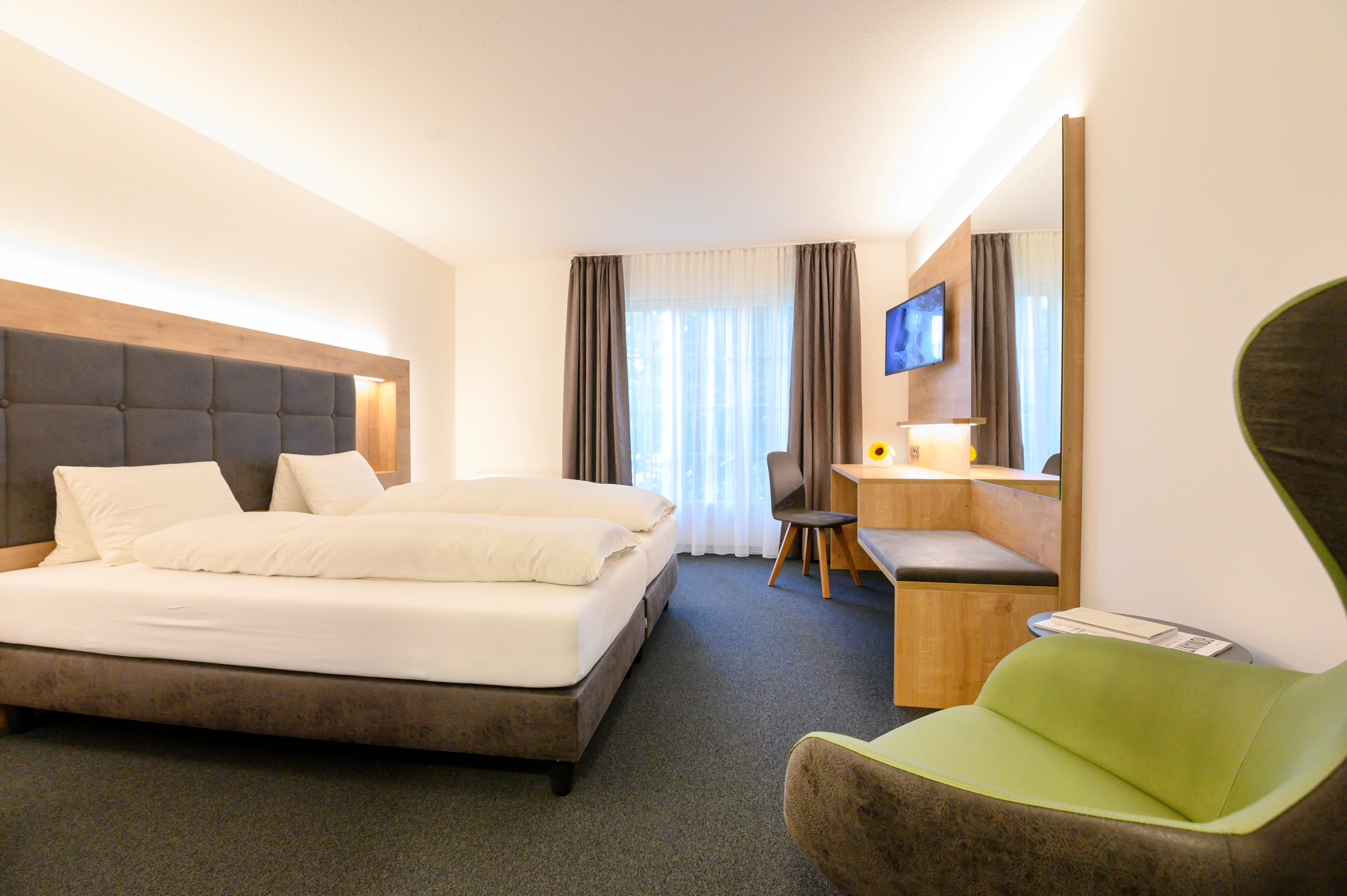 Camera d'albergo arredata in stile moderno con letto matrimoniale, scrivania, televisore e una comoda poltrona.