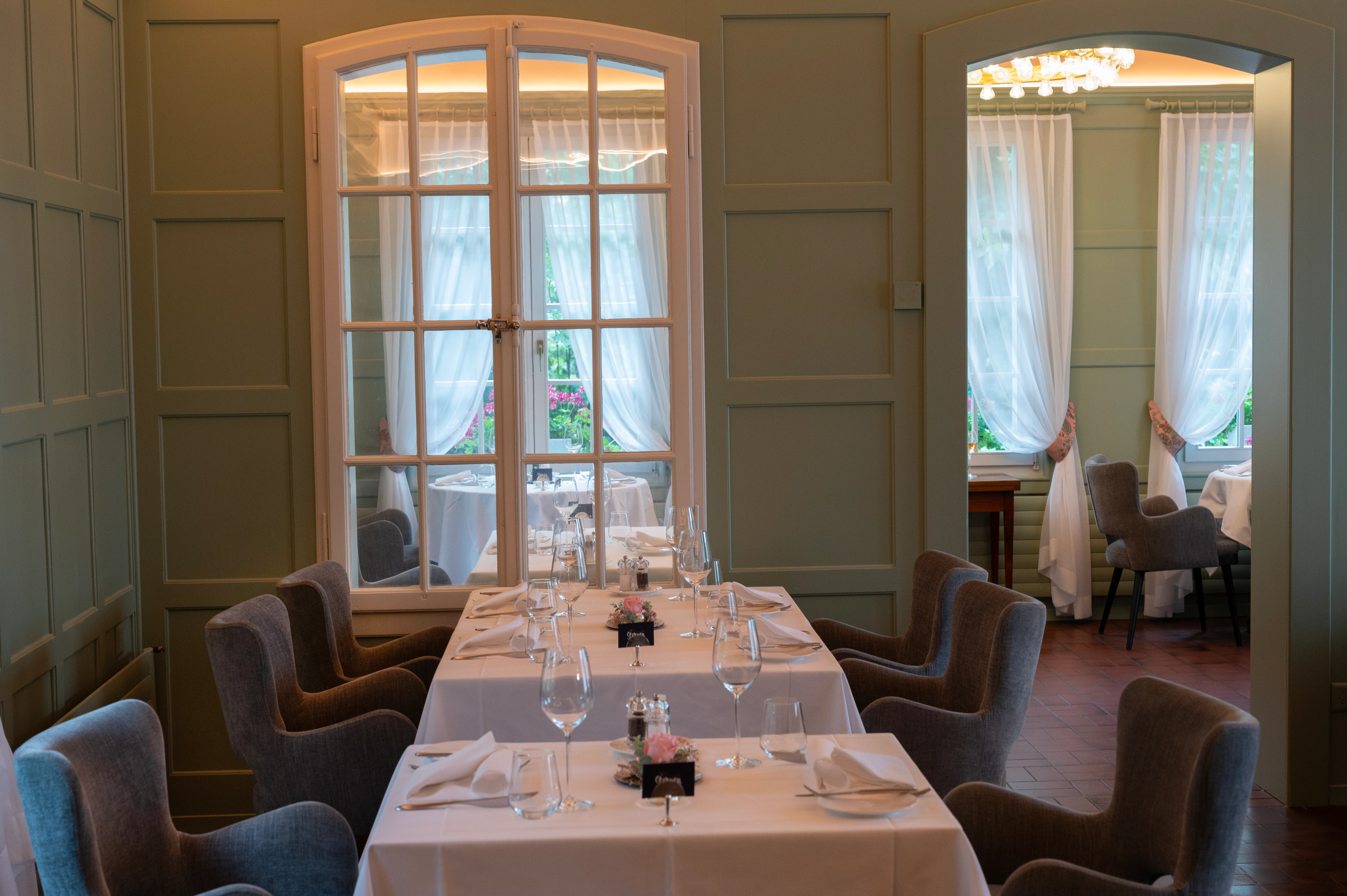 Tavolo da ristorante apparecchiato con stile al ristorante “Sterne”, con bicchieri, tovaglioli di stoffa e vista sulla sala adiacente.