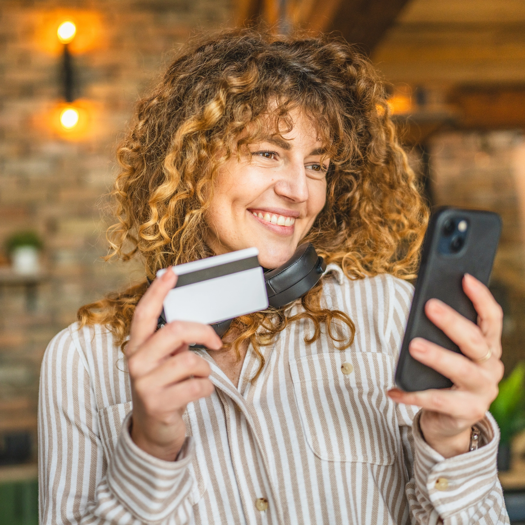 Eine Frau hält ihr Handy und ihre Kreditkarte in der Hand und lächelt.